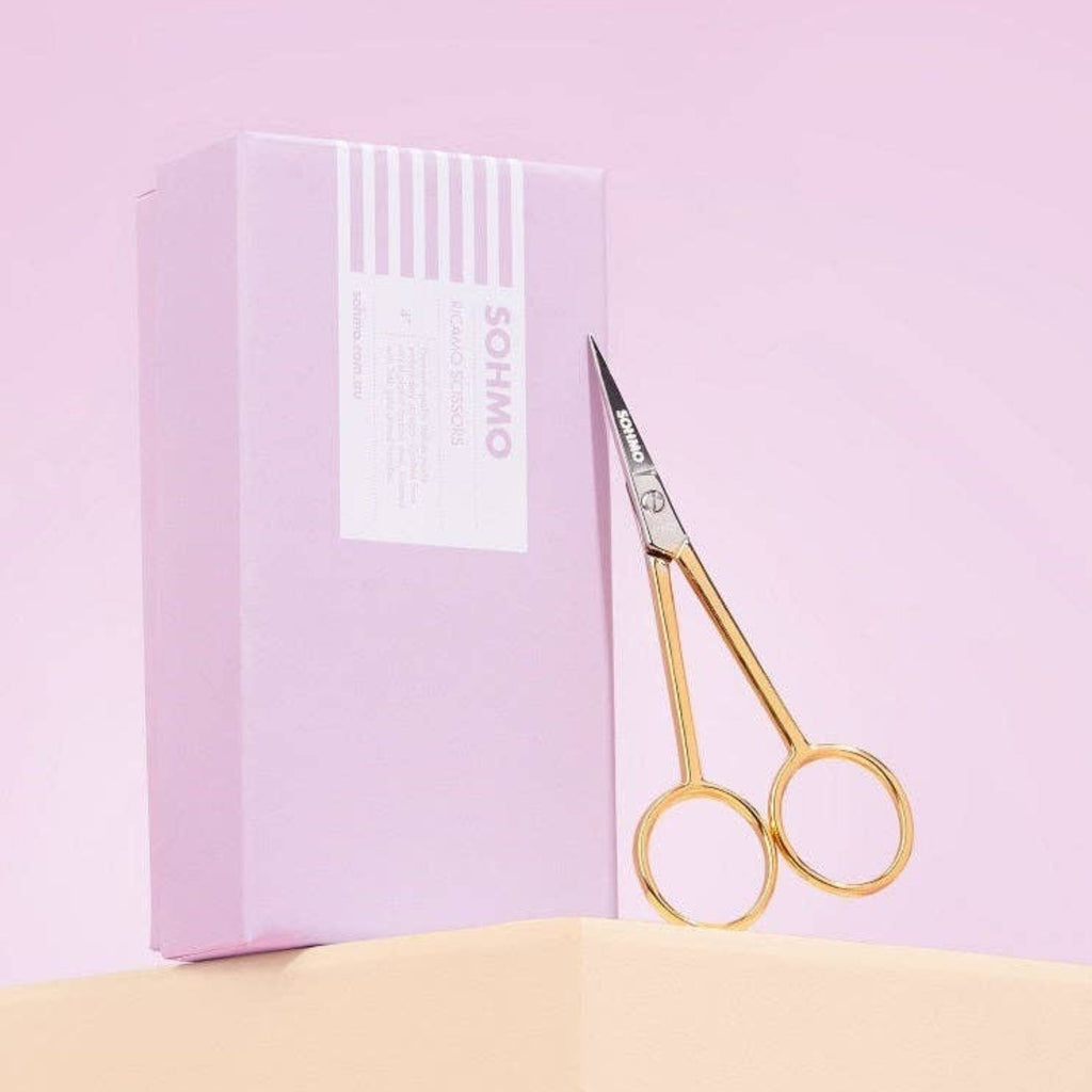 Gold scissors with a pink box on a light pink background