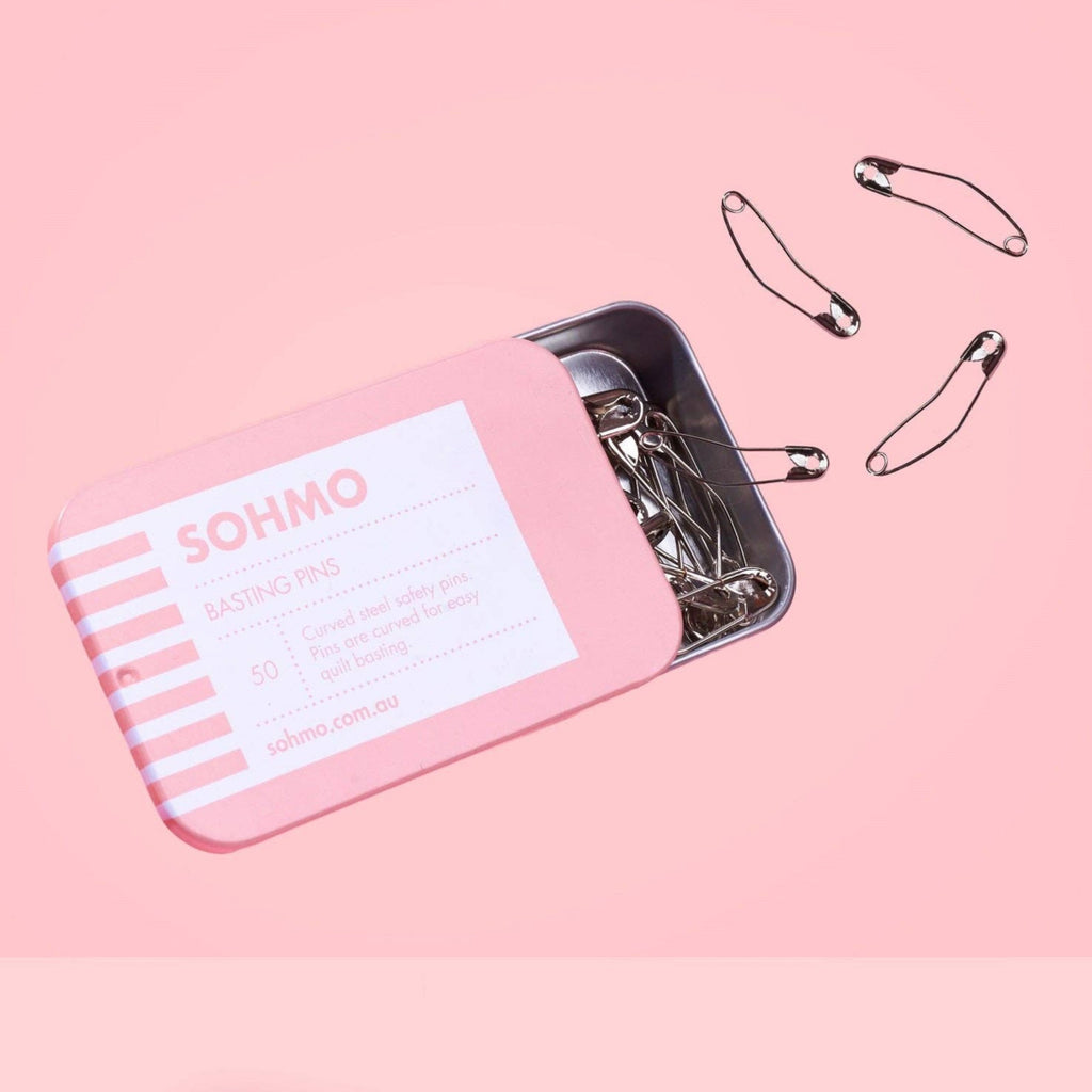 Pink tin box with safety pins on a pink background