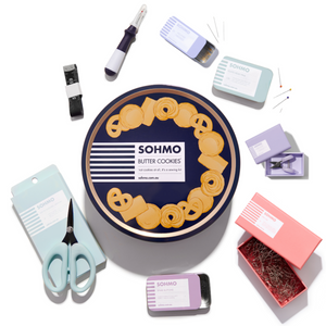 Collection of stationery items including a cookie-themed box, scissors, and various small containers on a white background.