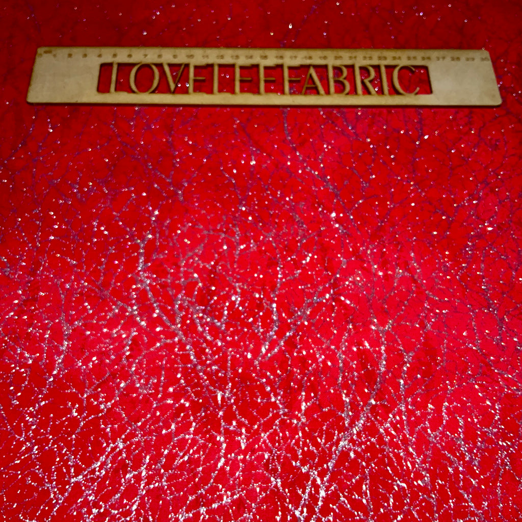 A close-up view of a red fabric with a textured silver metallic thread, showing the sparkle and detail of the material.